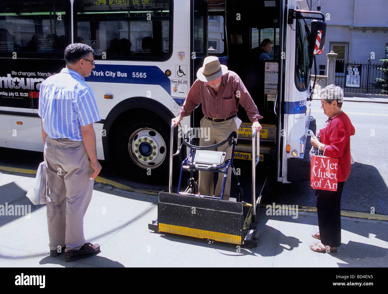 Disabled man getting off of a city bus using an orthopedic walker while socially distant pedestrians waiting to get on the bus watch Stock Photo