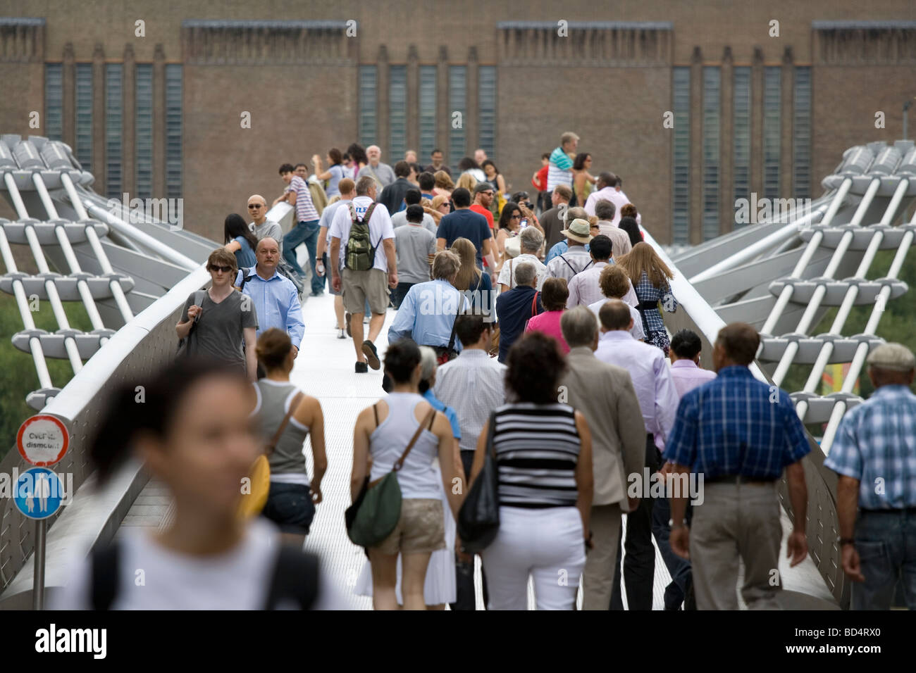 People cross the Millennium Bridge near the Tate Modern in London. Stock Photo