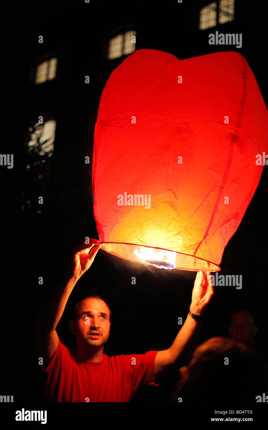 man launches sky lantern into the night sky; floating lantern Stock Photo