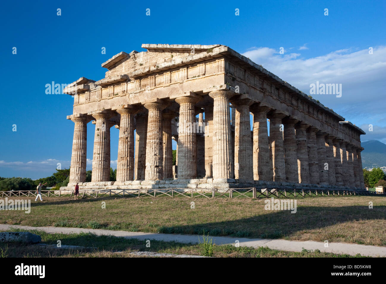 A couple strolls past the temple of Neptune at Paestum, viewed from the southwest. Stock Photo