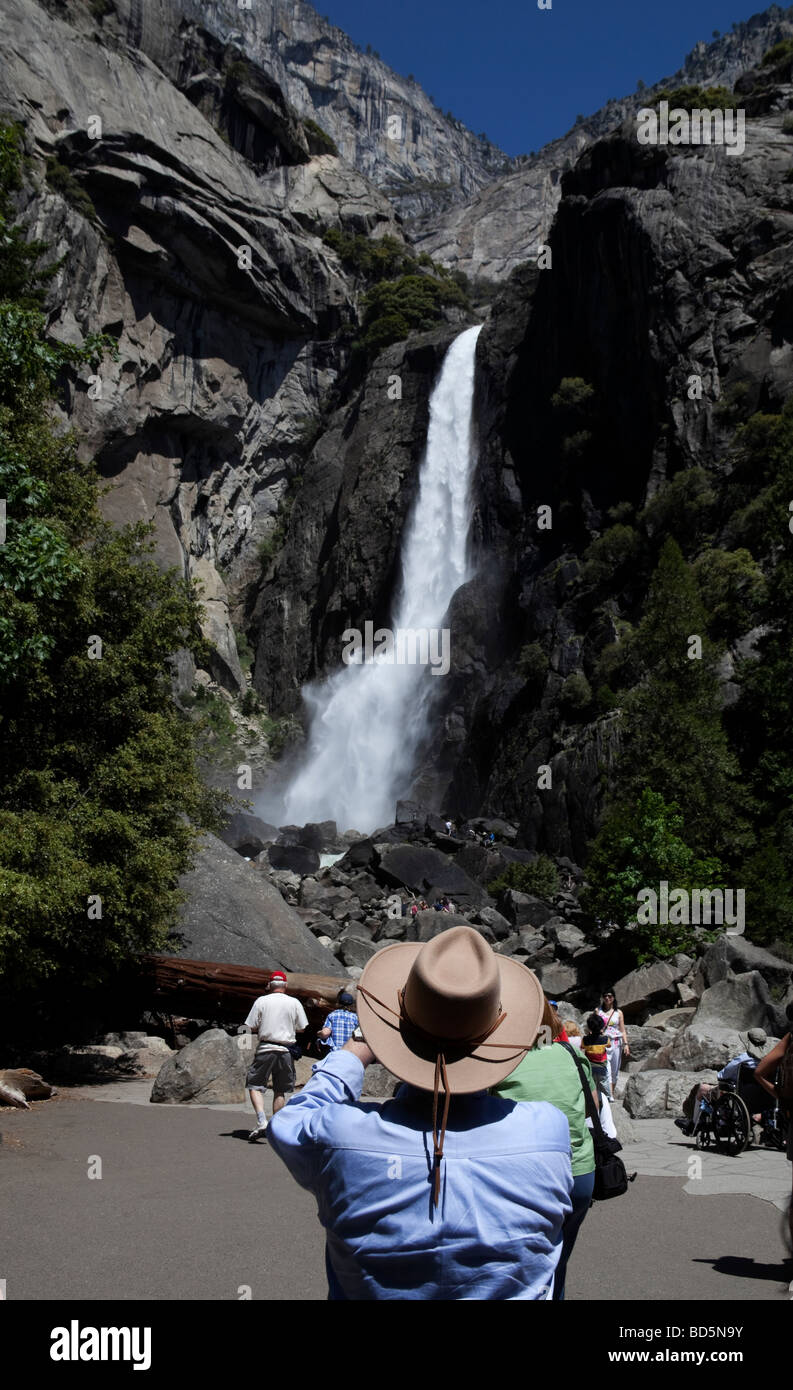 Man in foreground taking photograph of Yosemite lower falls National Park, California, USA Stock Photo