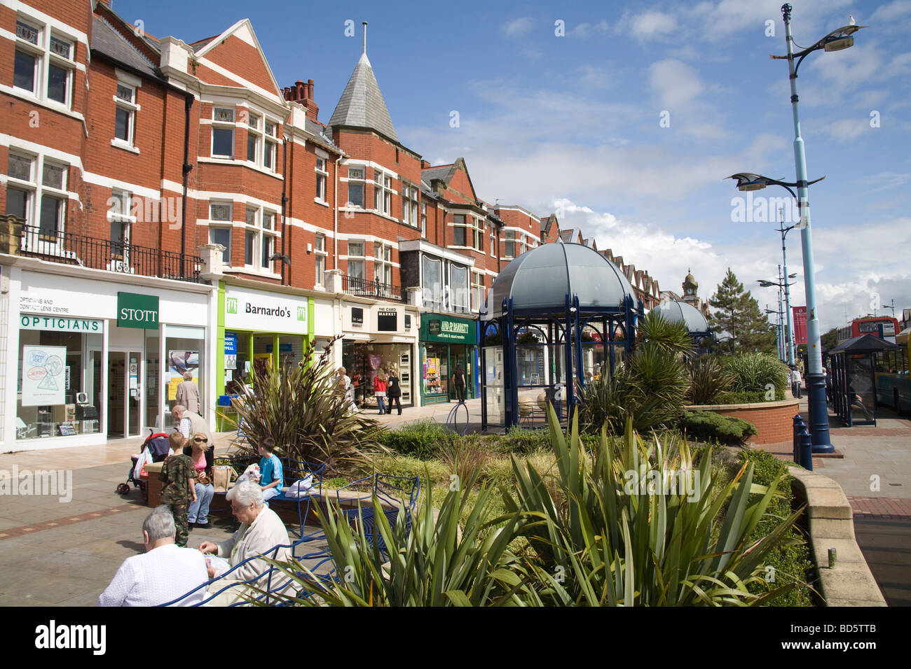 Lytham St Annes Lancashire England EU People sitting out in the sunshine on seats along Sty Annes Street West in front of shops Stock Photo