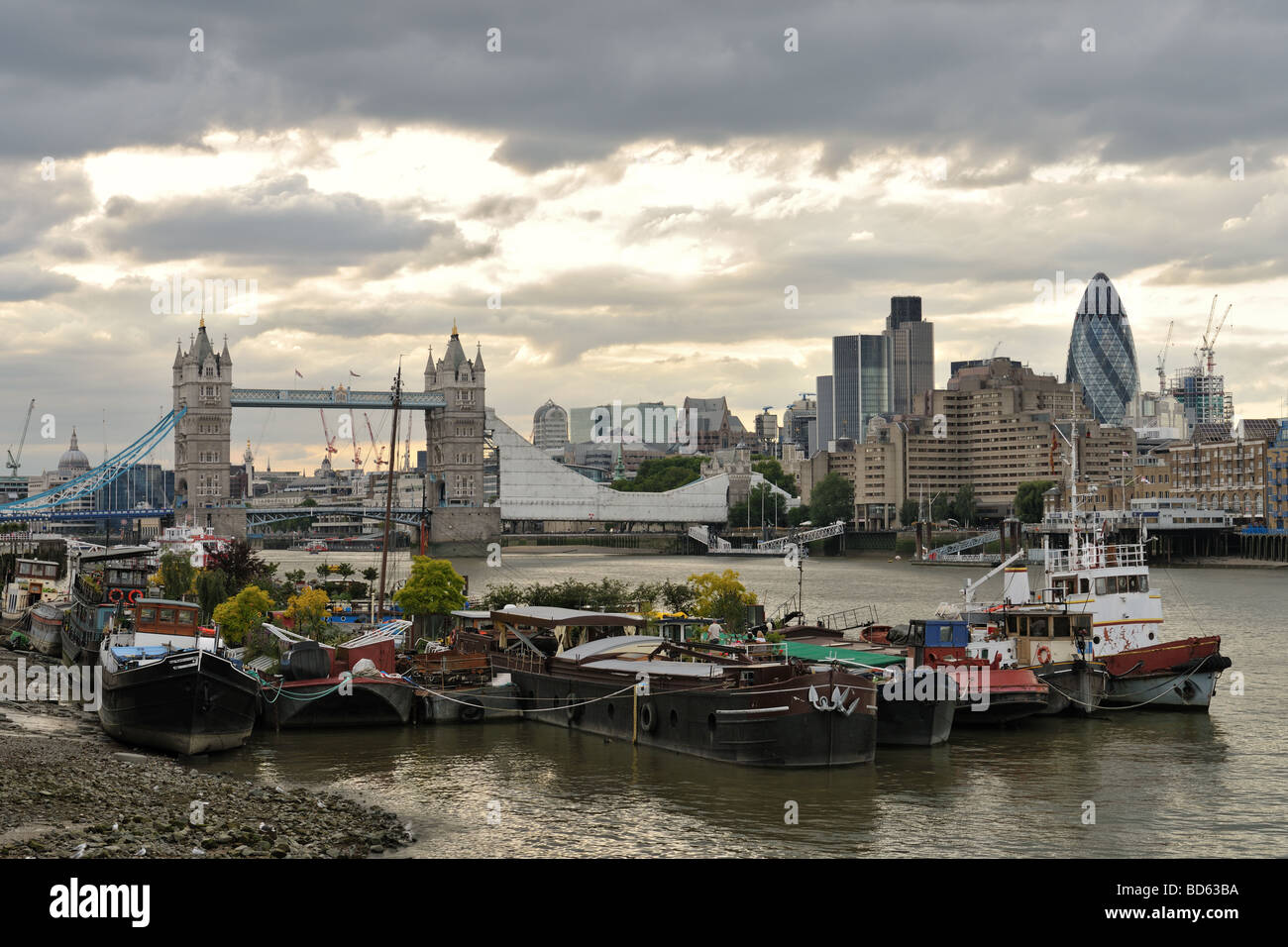 Houseboats moored on the south bank of the River Thames London with Tower Bridge and dramatic skiy in the background Stock Photo