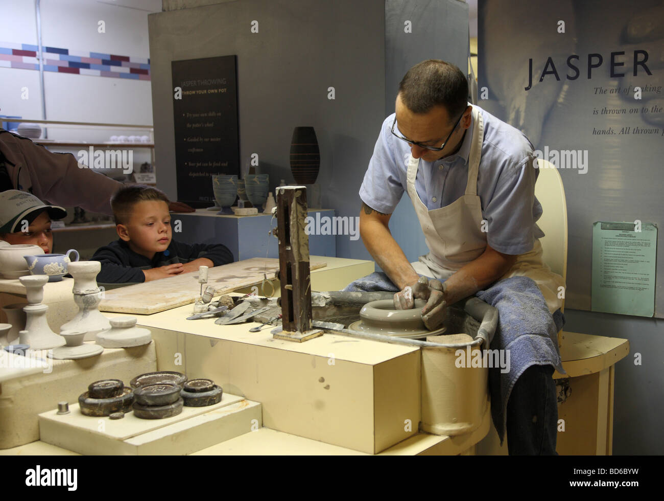 2 boys watching a potter throwing a pot on a potters wheel at the