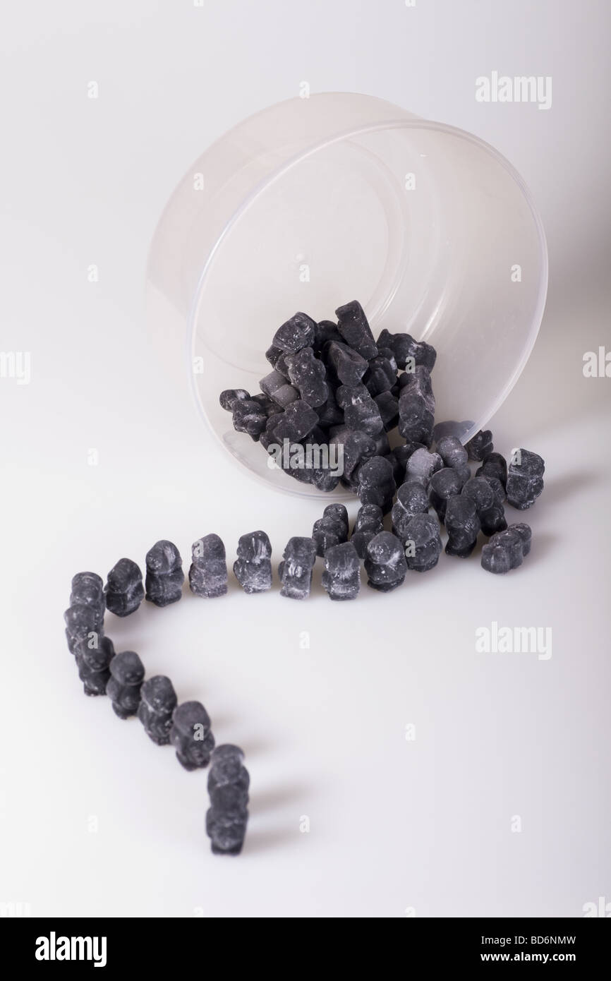 A trail of black jelly babies leaving a plastic container against a