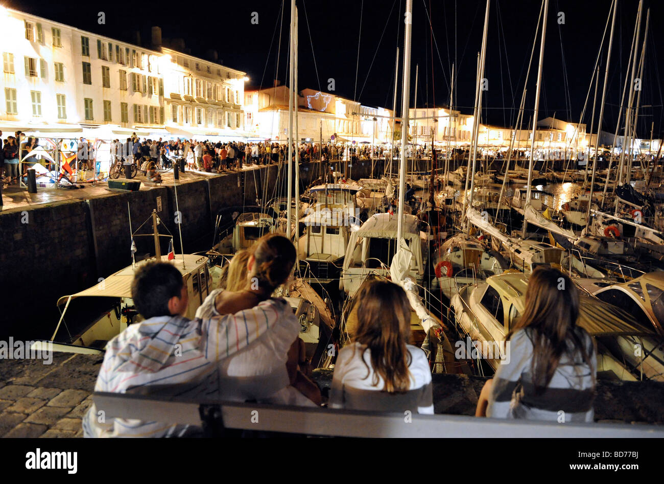 family of holidaymakers watch the crowds stroll along the harbourside on St Martin de Re Ile de re France Stock Photo