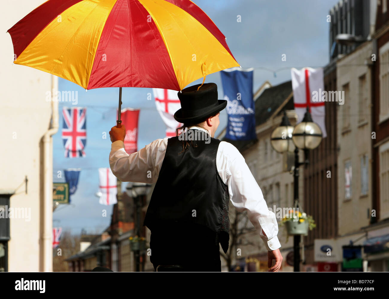 man on stilts holding umbrella on sunny day in English town Stock Photo