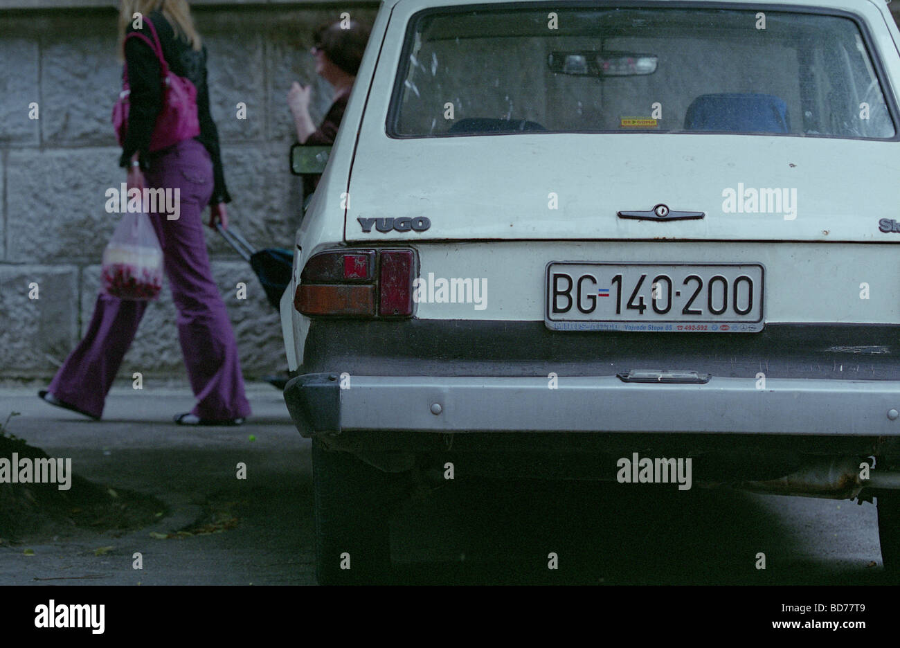 Parking white Yugo car with Belgrade license plate and pedestrians behind, Serbia, Balkans Stock Photo