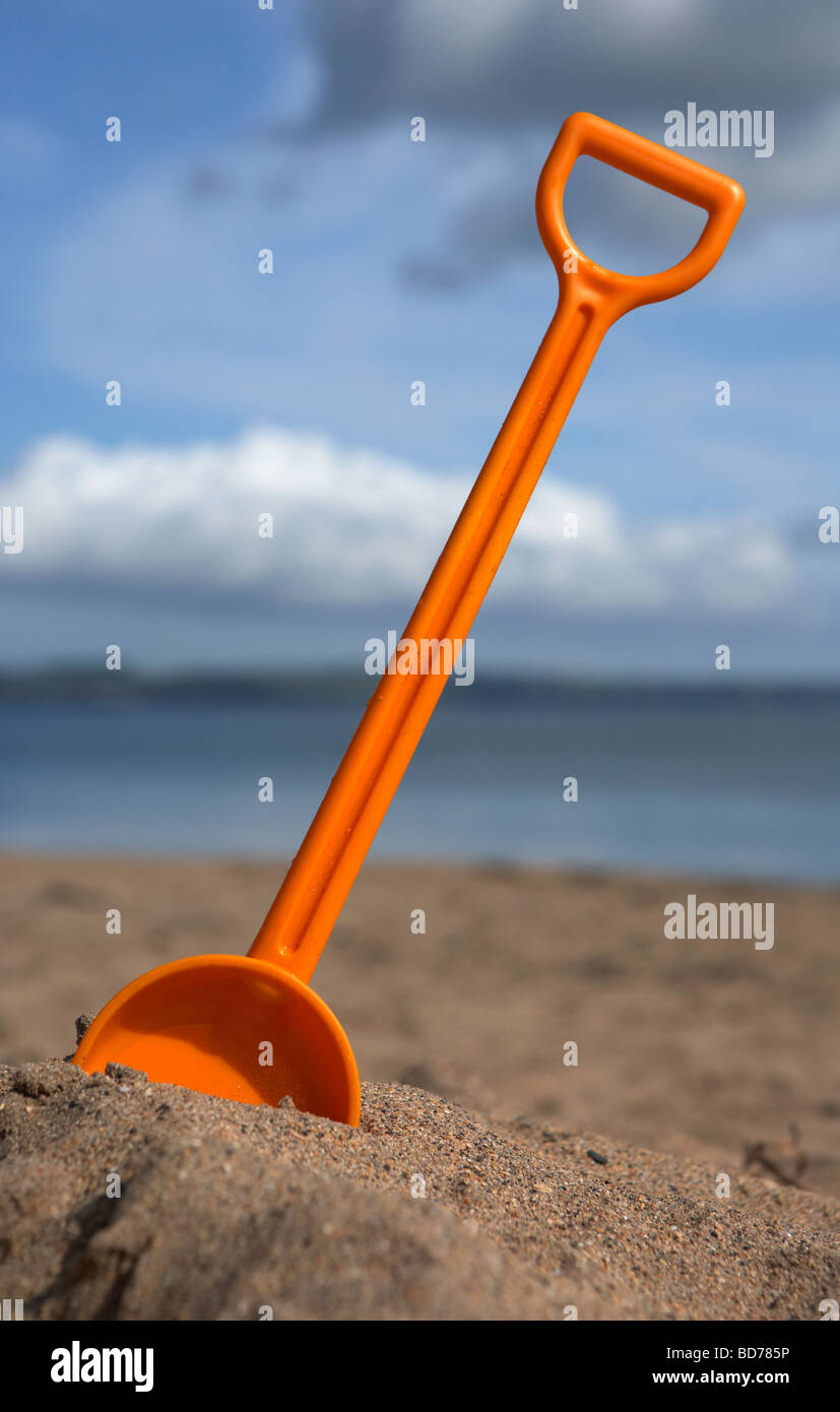 childs toy plastic spade stuck into the sand on a beach in the uk Stock Photo