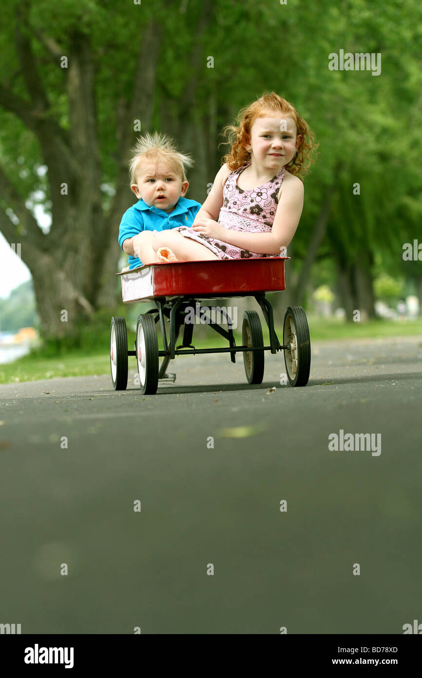 Brother and sister in red wagon at park Stock Photo - Alamy