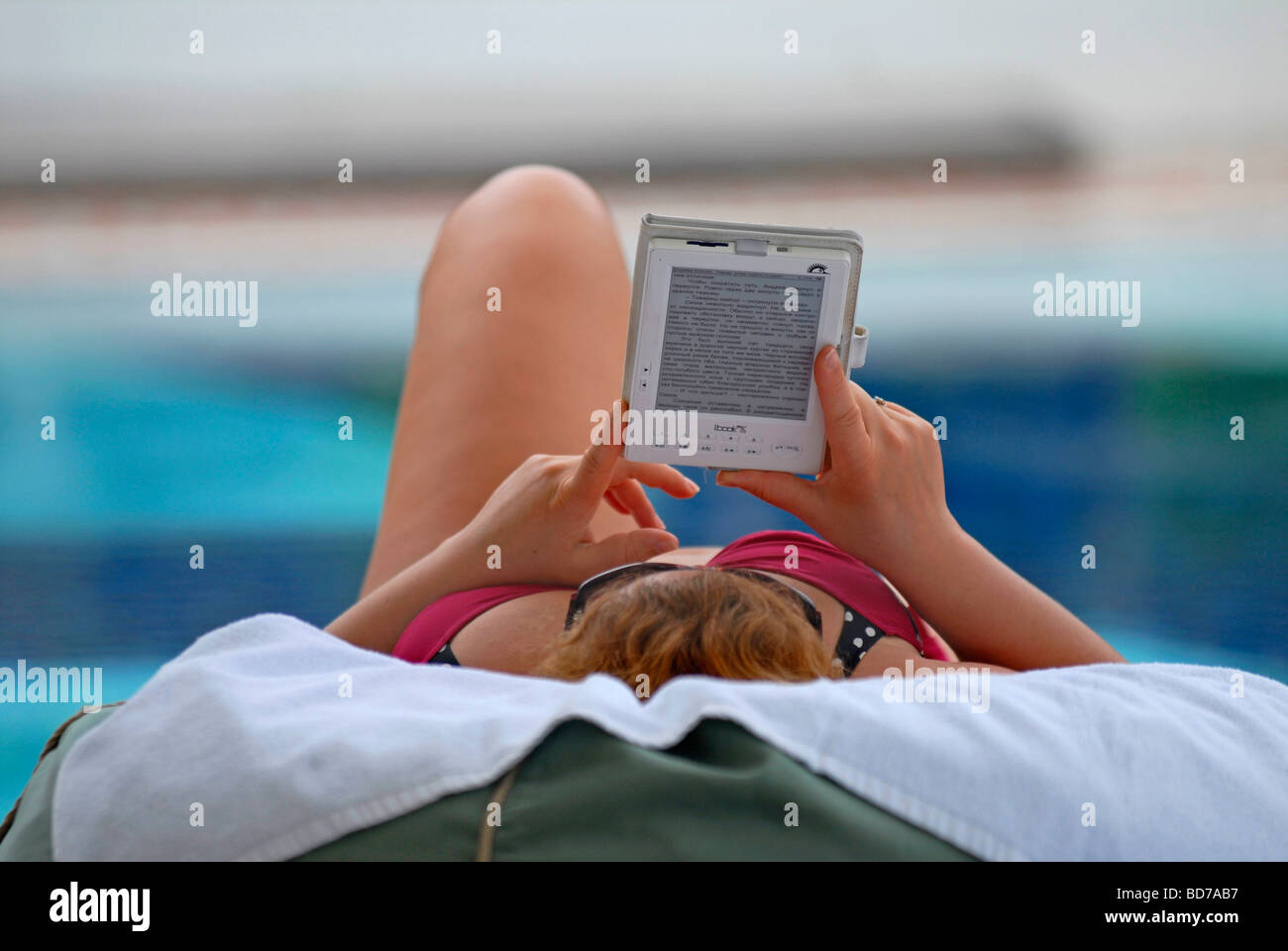 Woman at a hotel pool reading in an e-book, an electronic book Stock Photo