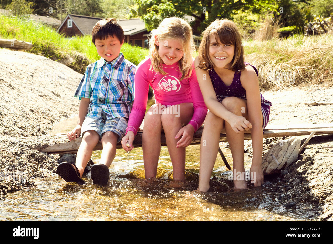 Children sitting on log bridge above creek Stock Photo