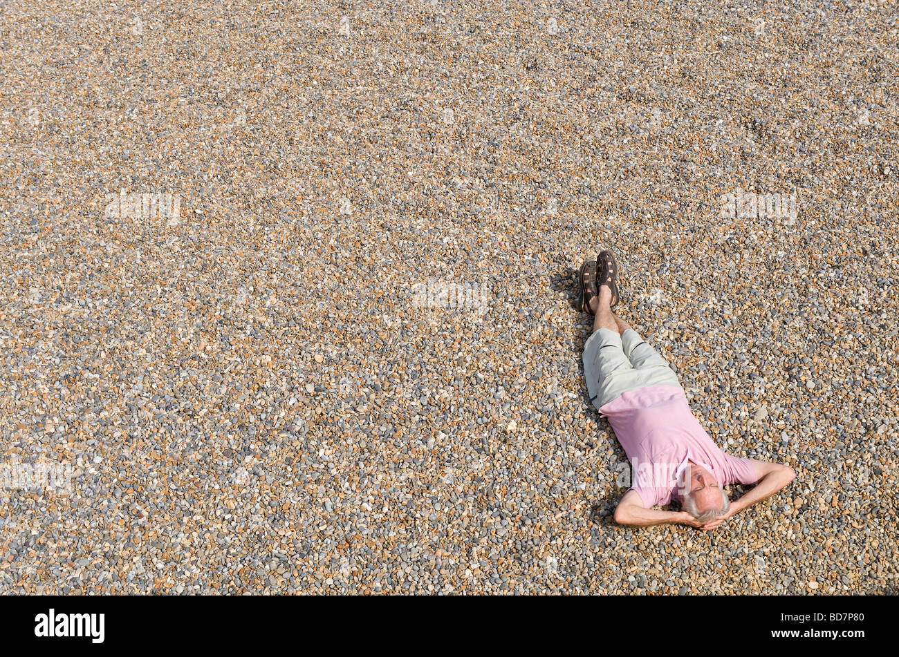 mature man laying on shingle beach Stock Photo