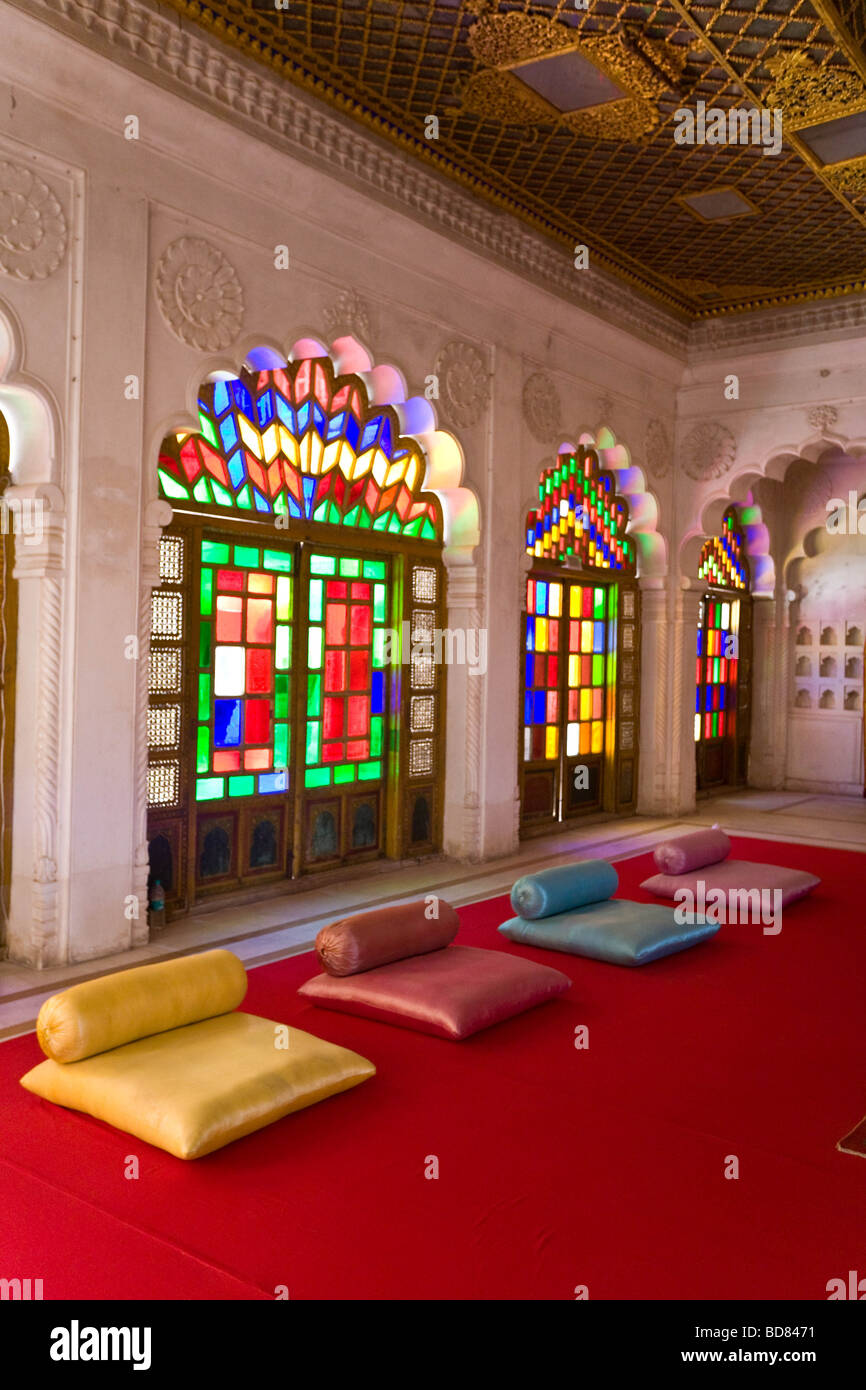 Gaudy room in the palace at Jodhpur with carved stonework and coloured glass above a red carpet and colourful cushions Stock Photo