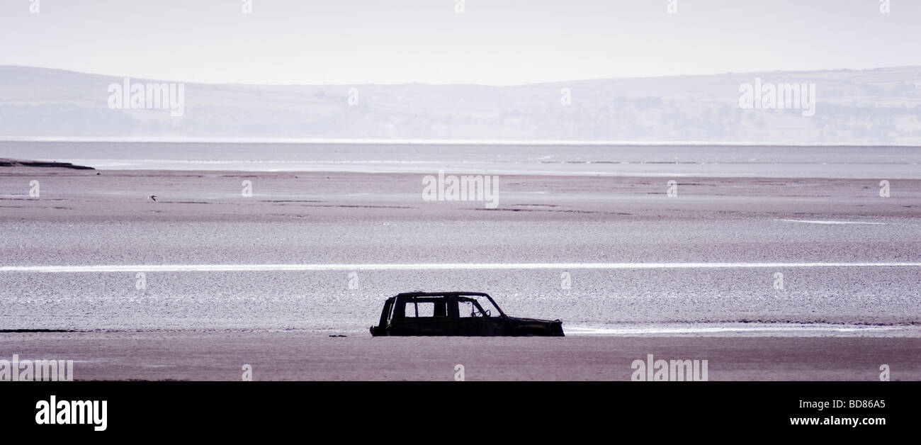 Silhouetted abandoned car partially submerged in the beach at Bolton-le-sands, Morecambe Bay. UK Stock Photo