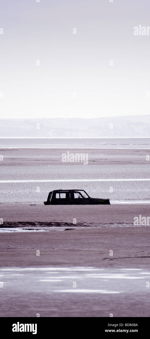 Silhouetted abandoned car partially submerged in the beach at Bolton-le-sands, Morecambe Bay. UK Stock Photo