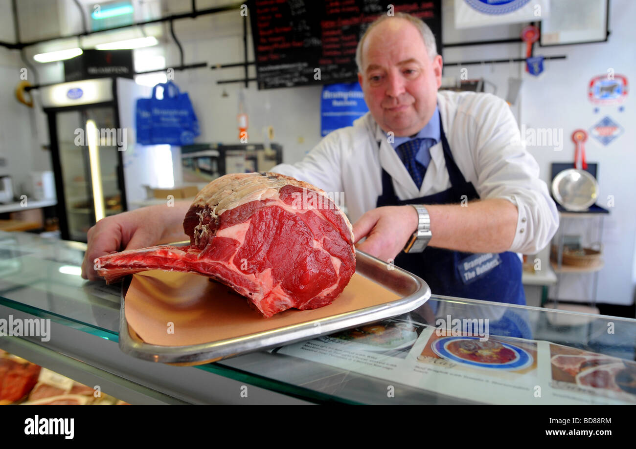 A butcher puts out a big joint of beef on the counter at at Bramptons a traditional butchers in Kemp Town Brighton Stock Photo