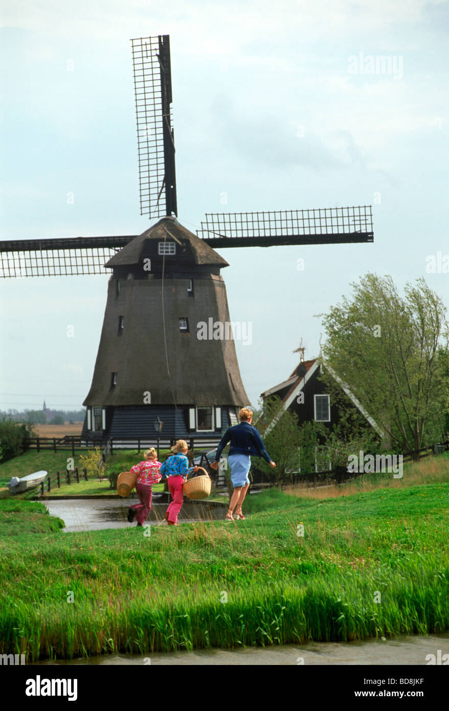 Mother and children with baskets walking home on pathway in Holland near windmill and canal Stock Photo