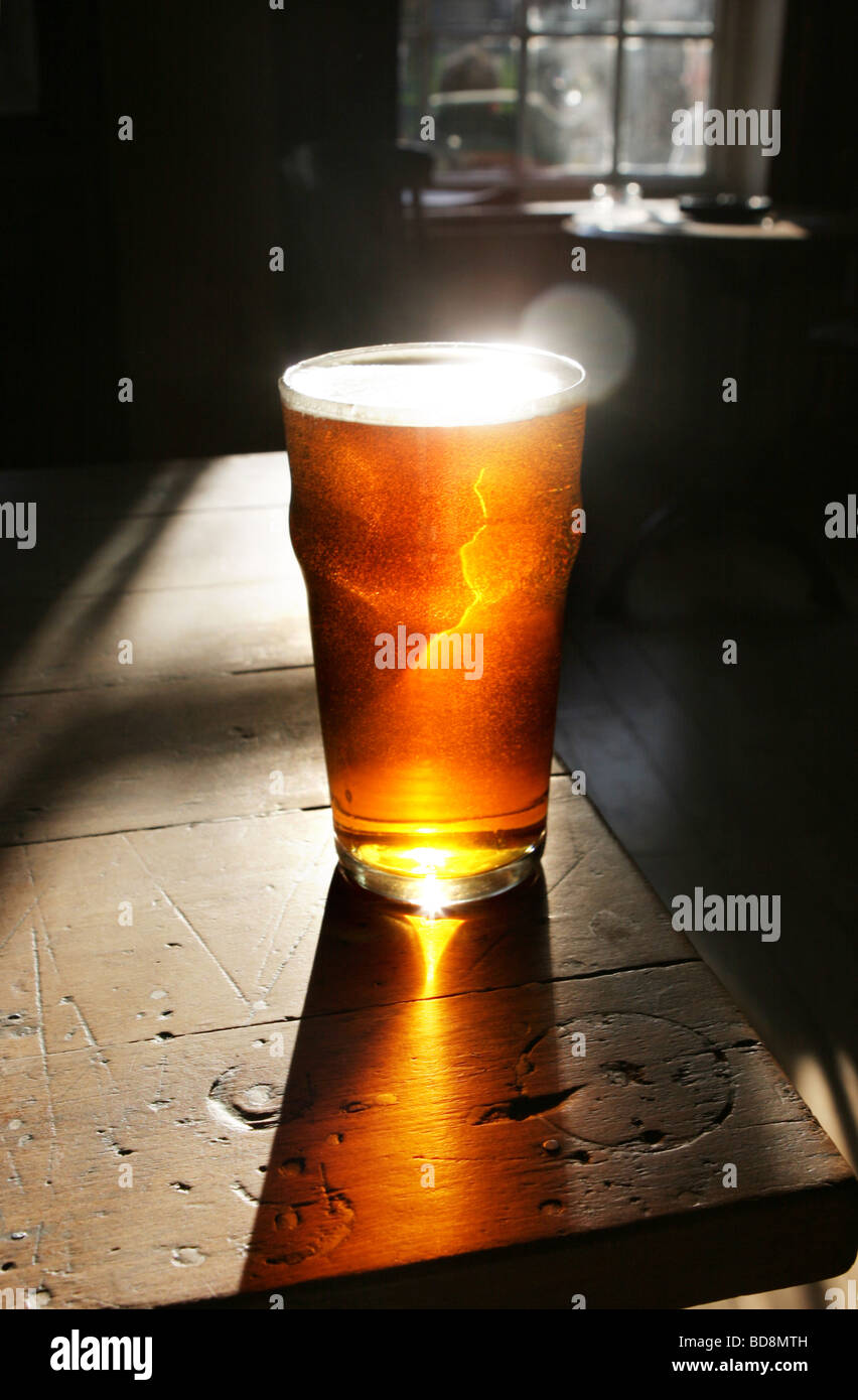 A pint of real ale on a traditional wooden bar inside a pub with sunlight streaming through the window Stock Photo