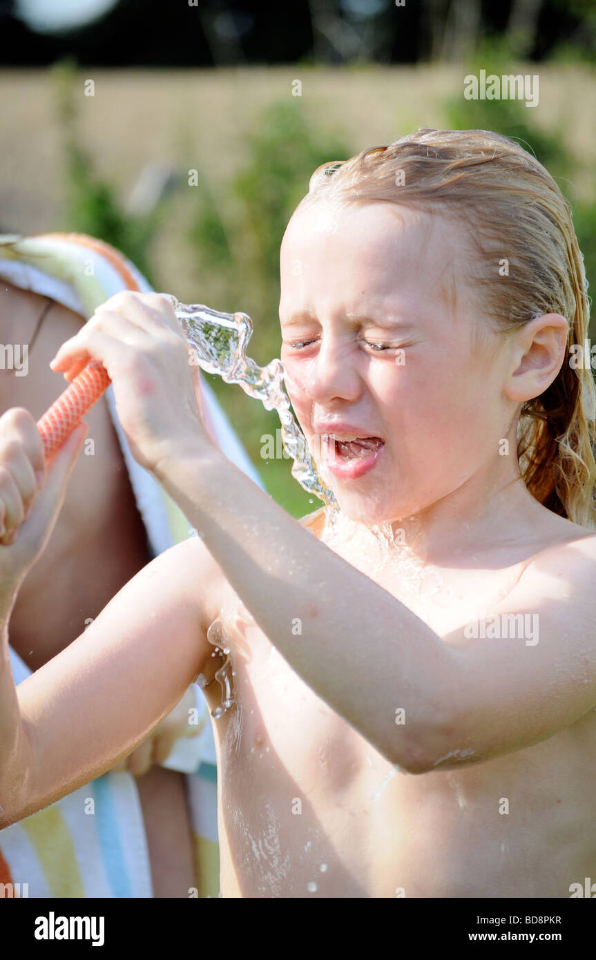Photograph of a girl washing and cooling with hose pipe water on a summer day in British garden UK Stock Photo