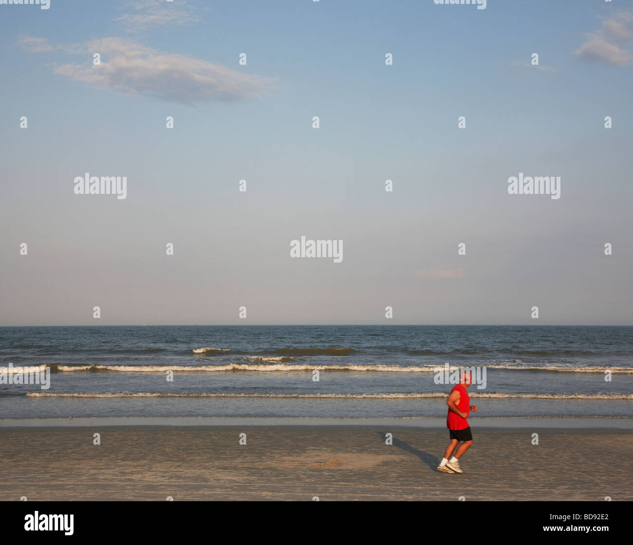 Man jogging in the evening sun along beach listening to music on his headphones Stock Photo