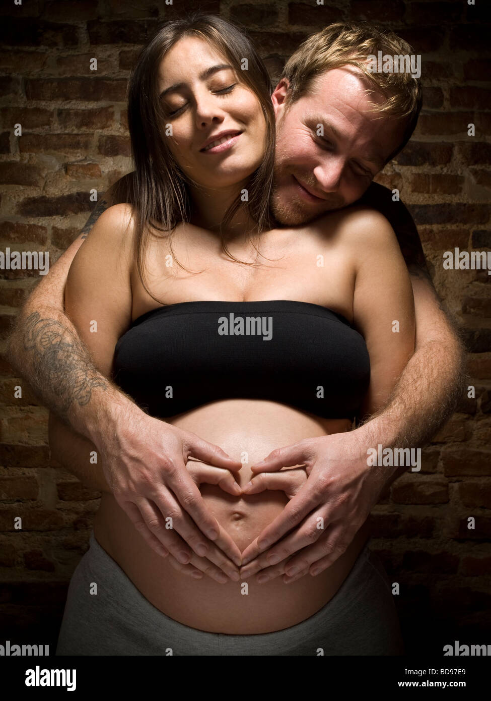 A young couple holding the pregnant belly and making a hard shape with their hands. Stock Photo