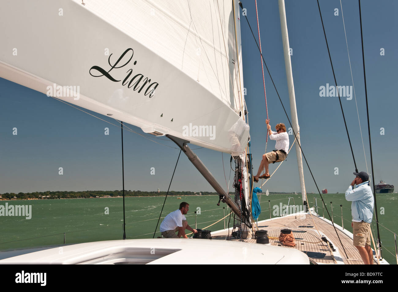 Crew adjusting the main on the foredeck of sailing yacht Liara as she sails down Southampton Water Stock Photo