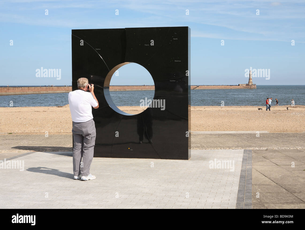 Man taking a photograph of Roker lighthouse through a monolithic granite structure aligned with the stars of the solar system, England, UK Stock Photo