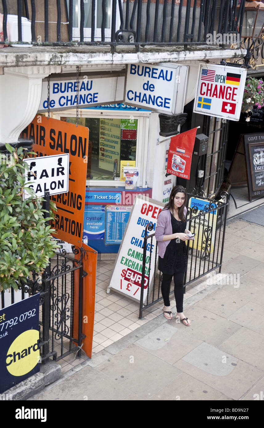 High angle of young woman standing outside a Bureau De Change amid promotional signs Stock Photo