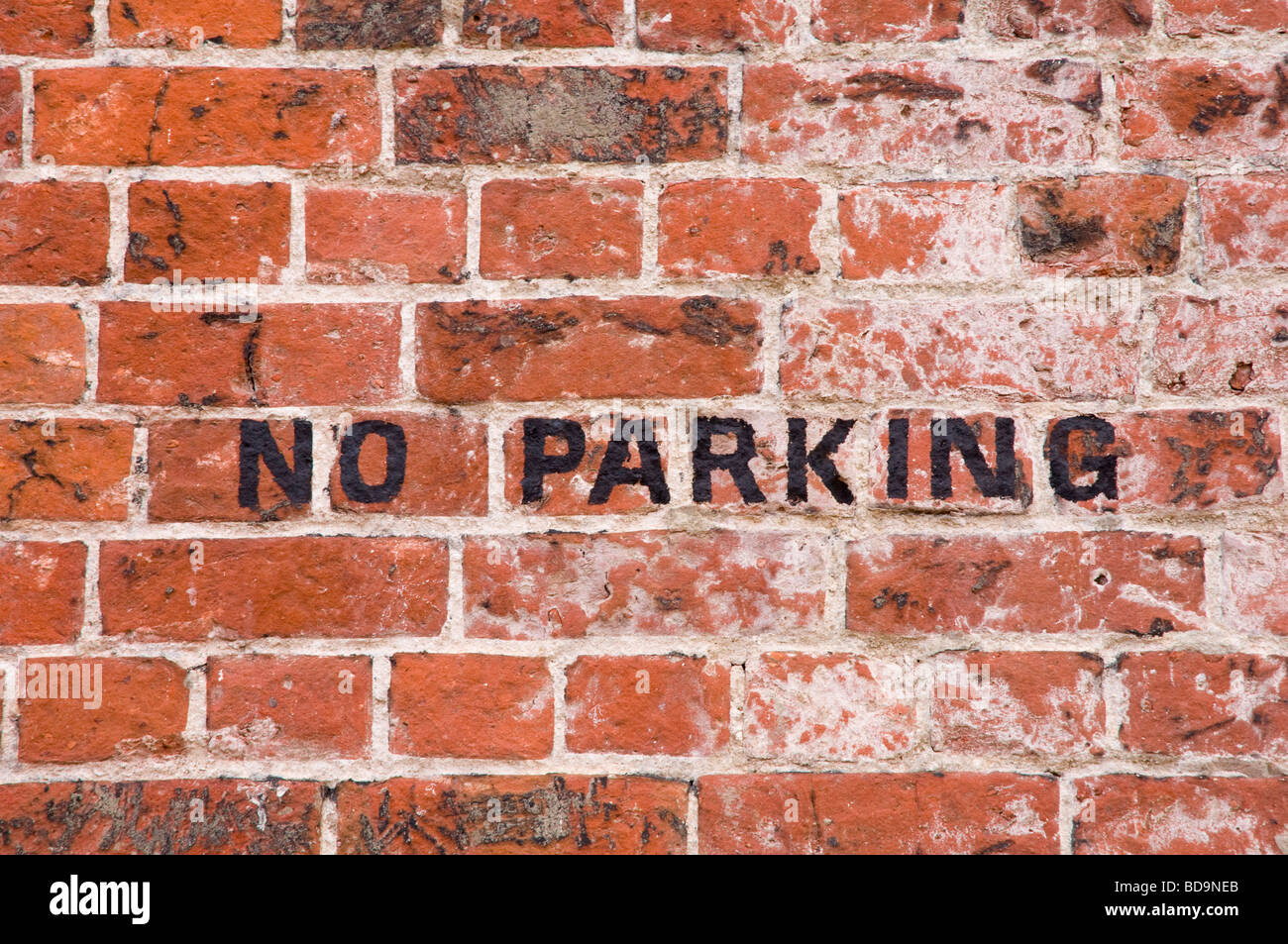 No Parking - signage painted in black on a red brick wall. UK Stock Photo