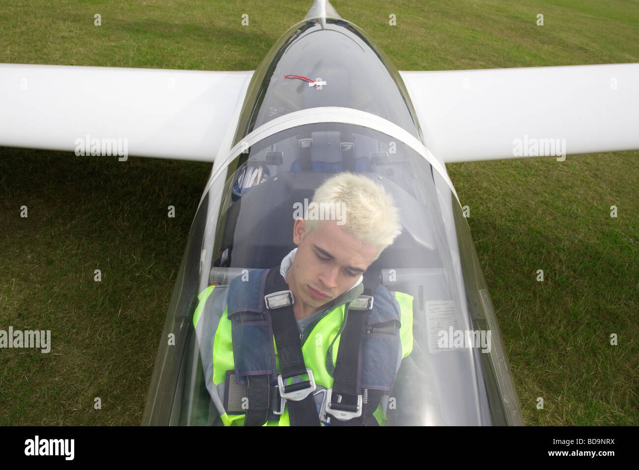 A young teenage pilot with bleach blond hair strapped into the cockpit of a glider anxiously awaiting takeoff Stock Photo