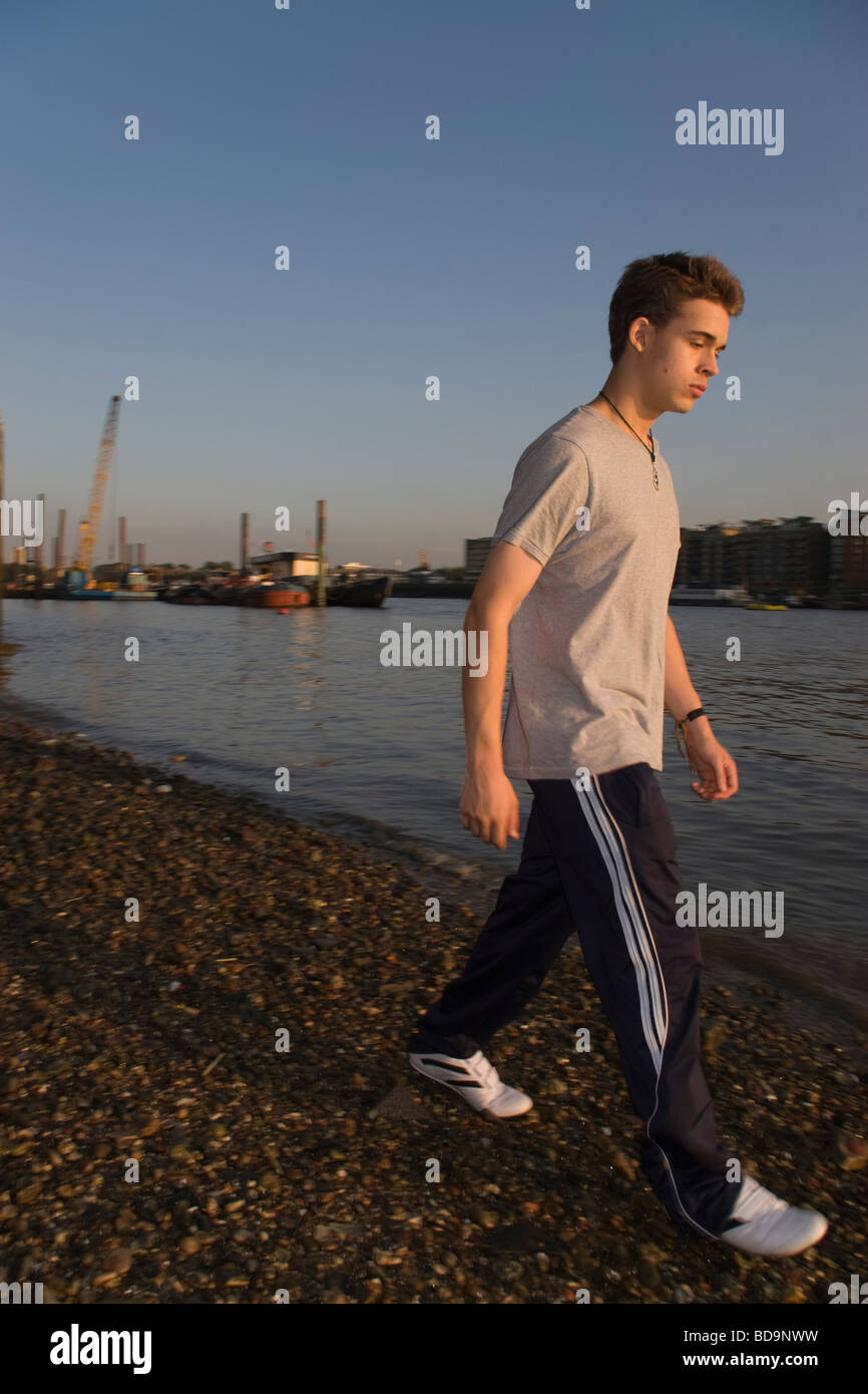Teenage boy walking briskly along the waters edge of the River Thames in London at dusk Stock Photo