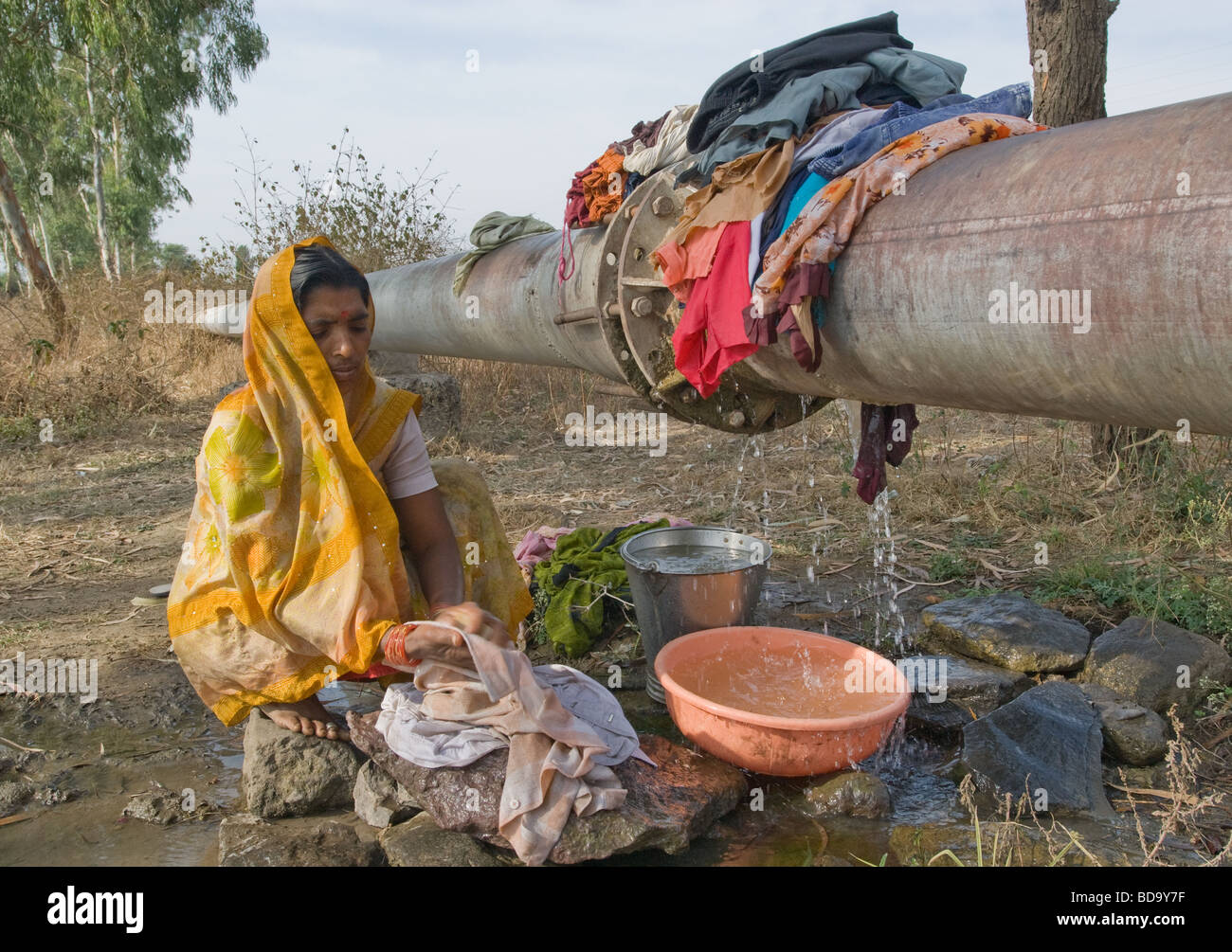 Women washing clothes using water from a leaking pipeline along the