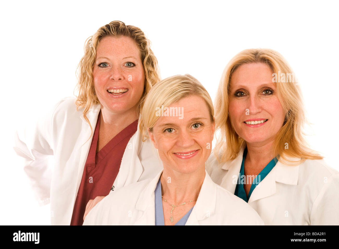team of three happy and confident female doctors or nurses medical personnel wearing colorful scrubs clothes and white lab coats Stock Photo