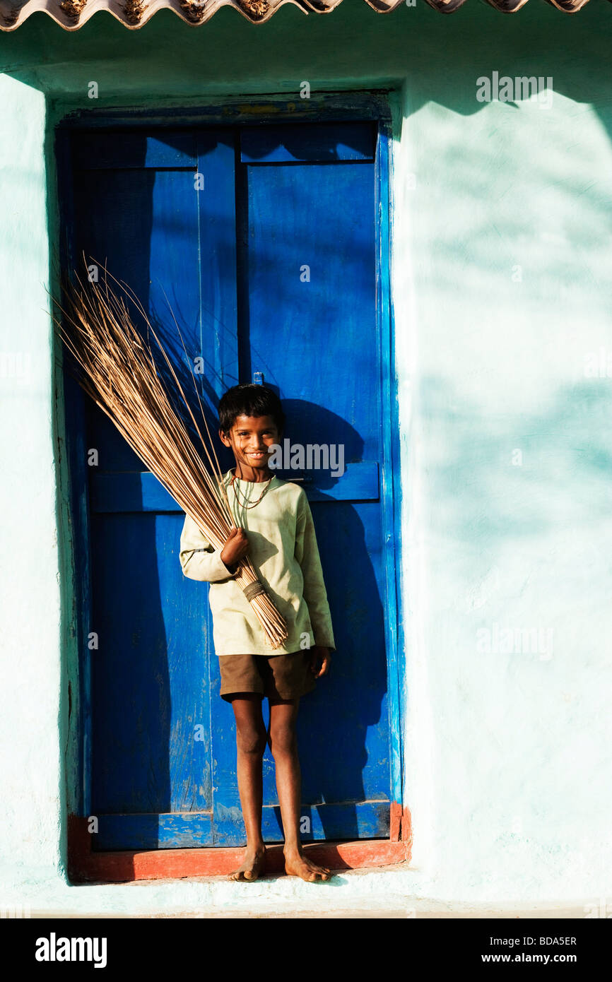 Boy standing with a broom in front of a door, Hampi, Karnataka, India