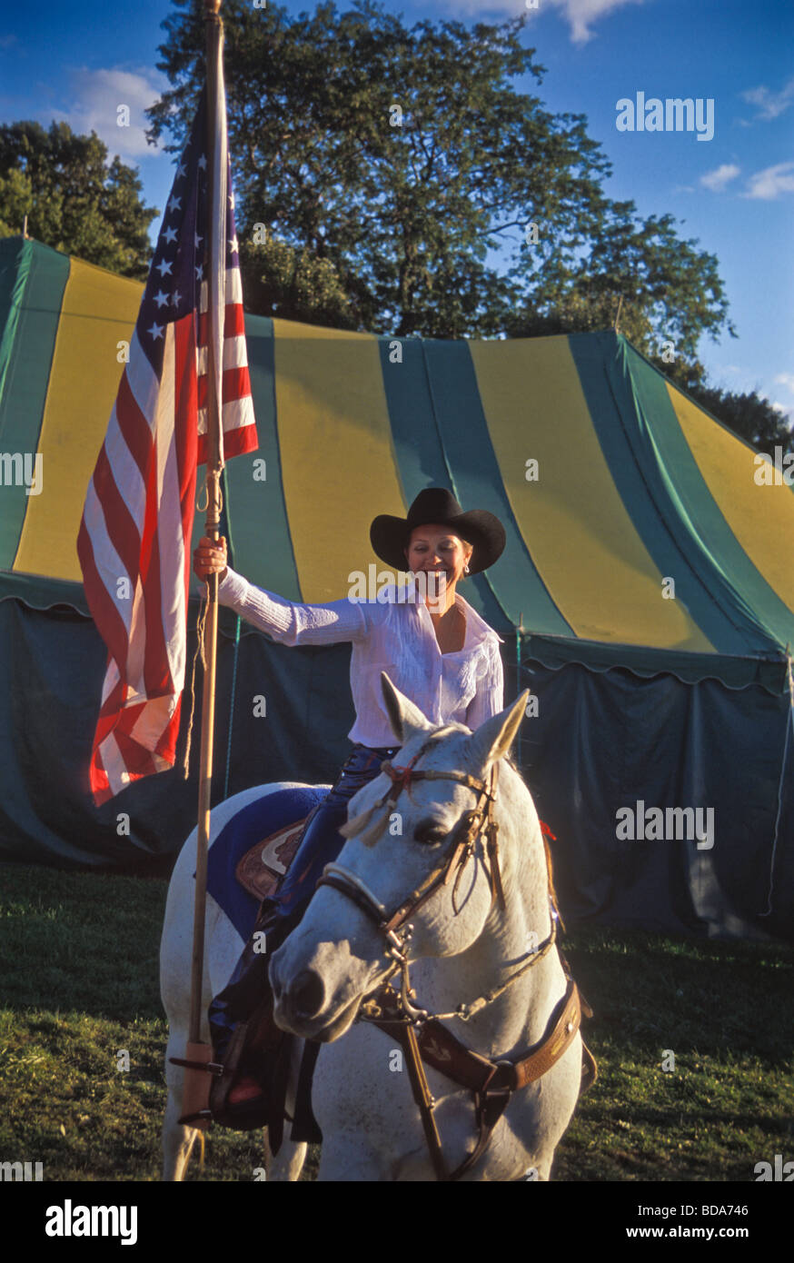 Young woman on white horse carries American flag at opening ceremony of county fair rodeo Stock Photo