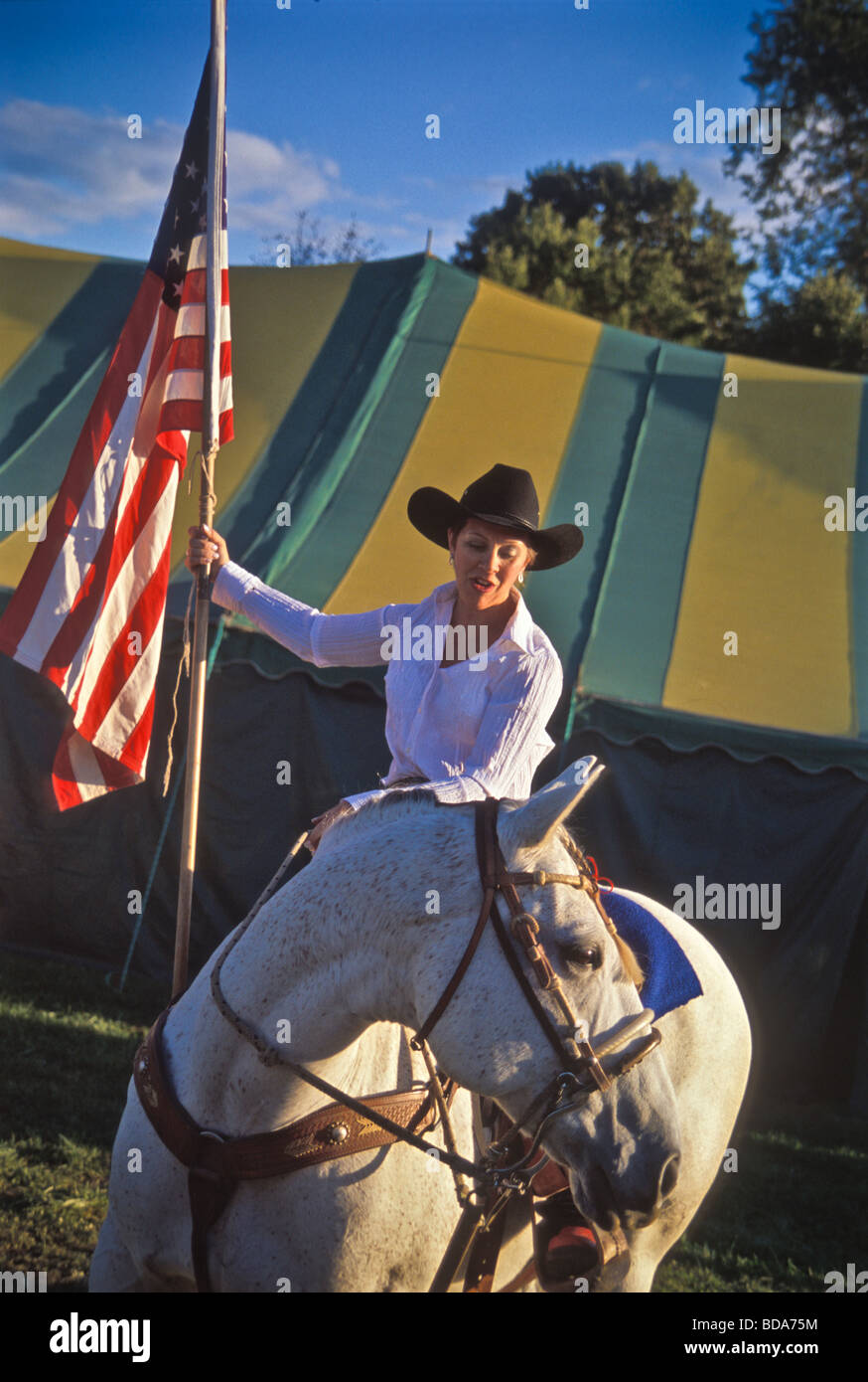 Young woman on white horse carries American flag at opening ceremony of county fair rodeo Stock Photo