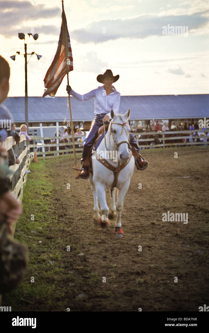 Young woman on white horse carries American flag at opening ceremony of county fair rodeo Stock Photo