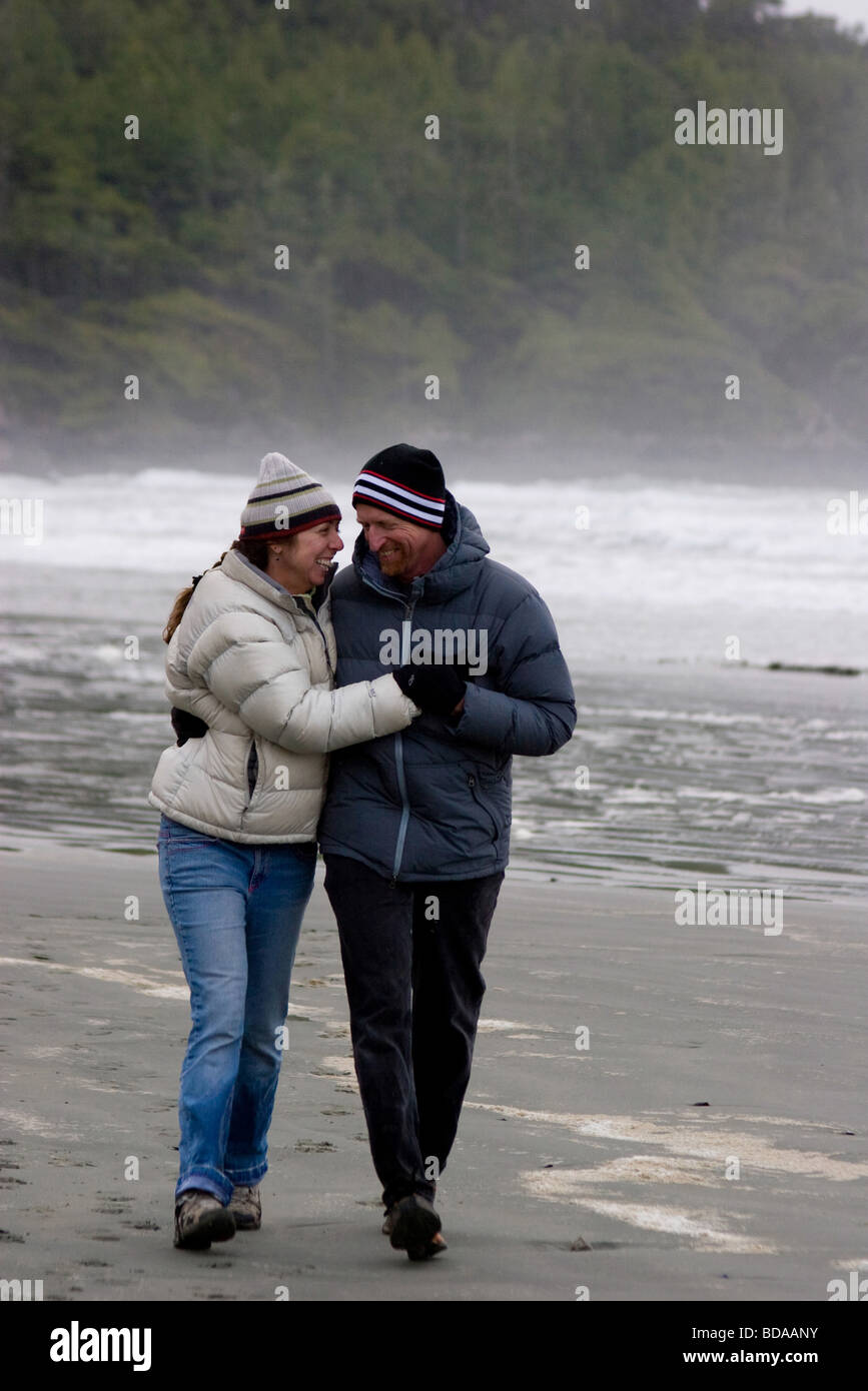 Couple walking arm in arm on the beach in winter gear, near Tofino, BC Stock Photo