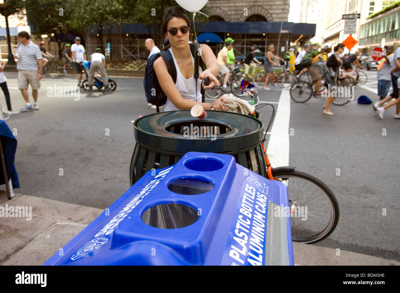 A woman throws her paper cup into a trash can next to a recycling bin ...