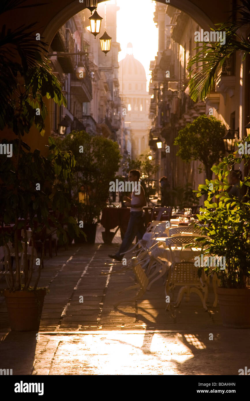 Late afternoon light streams in through archway into outdoor restaurant in Old Havana as man walks through Stock Photo