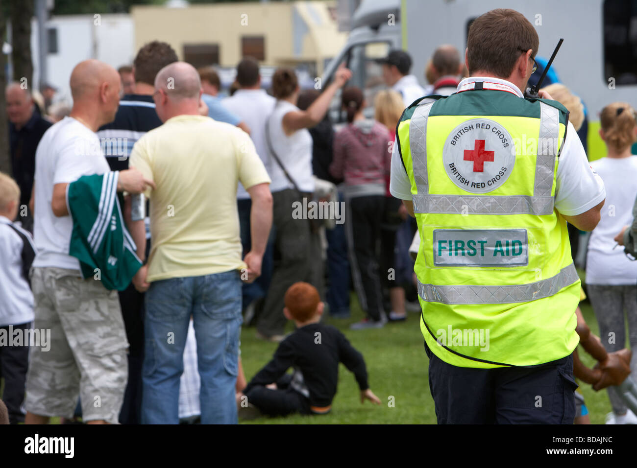 member of the british red cross first aid team on the radio walking through a crowd at an outdoor event in belfast Stock Photo
