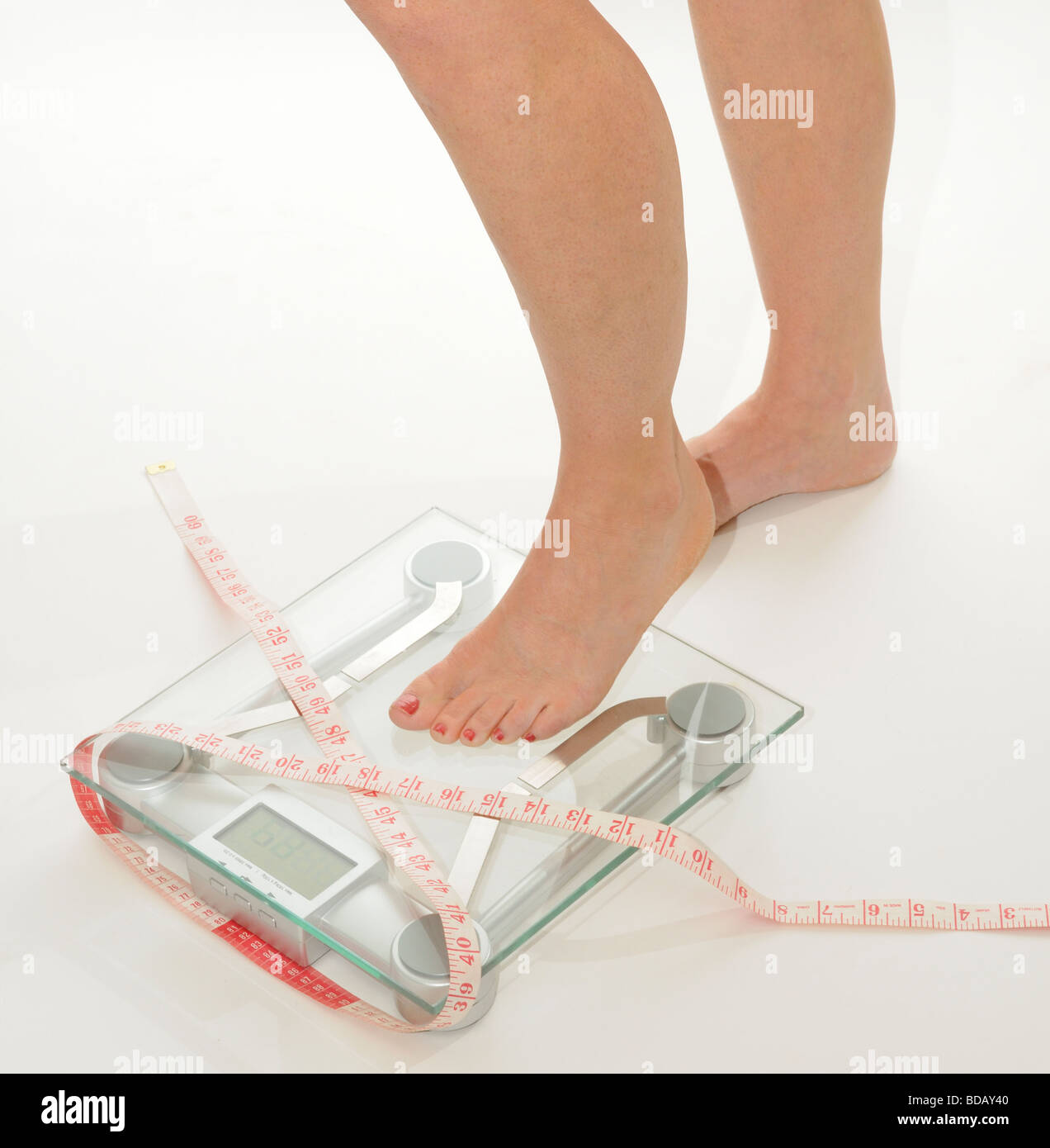 female legs and feet on bathroom scales draped with a tape measure Stock Photo