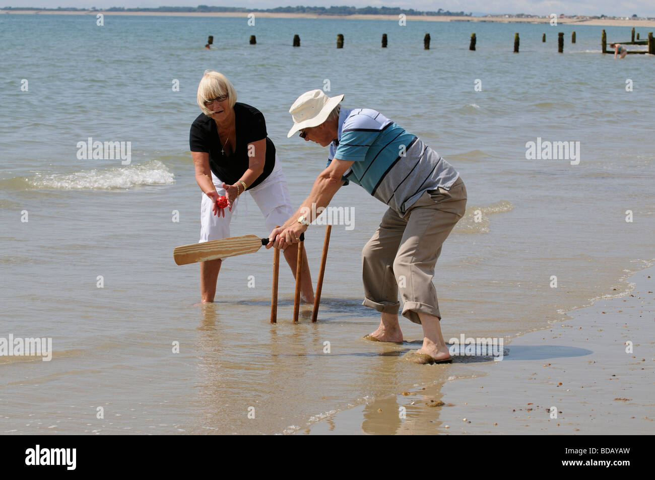 Man and woman playing cricket at the seaside retired couple enjoying