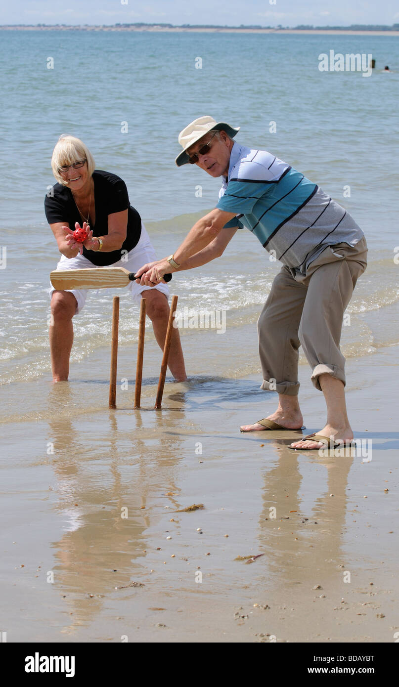 Man and woman playing cricket at the seaside retired couple enjoying
