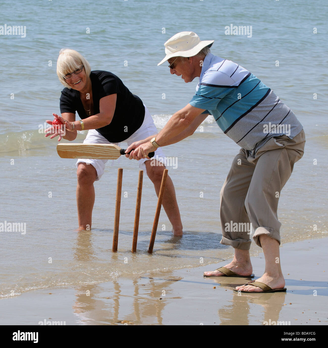 Man and woman playing cricket at the seaside retired couple enjoying