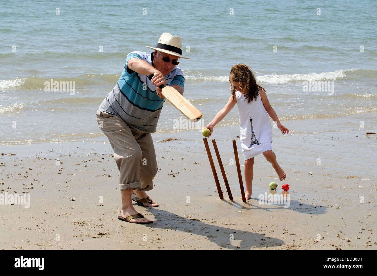 Grandparent playing a game of cricket on the beach with grandchild Grandaughter stumps her grandad Stock Photo