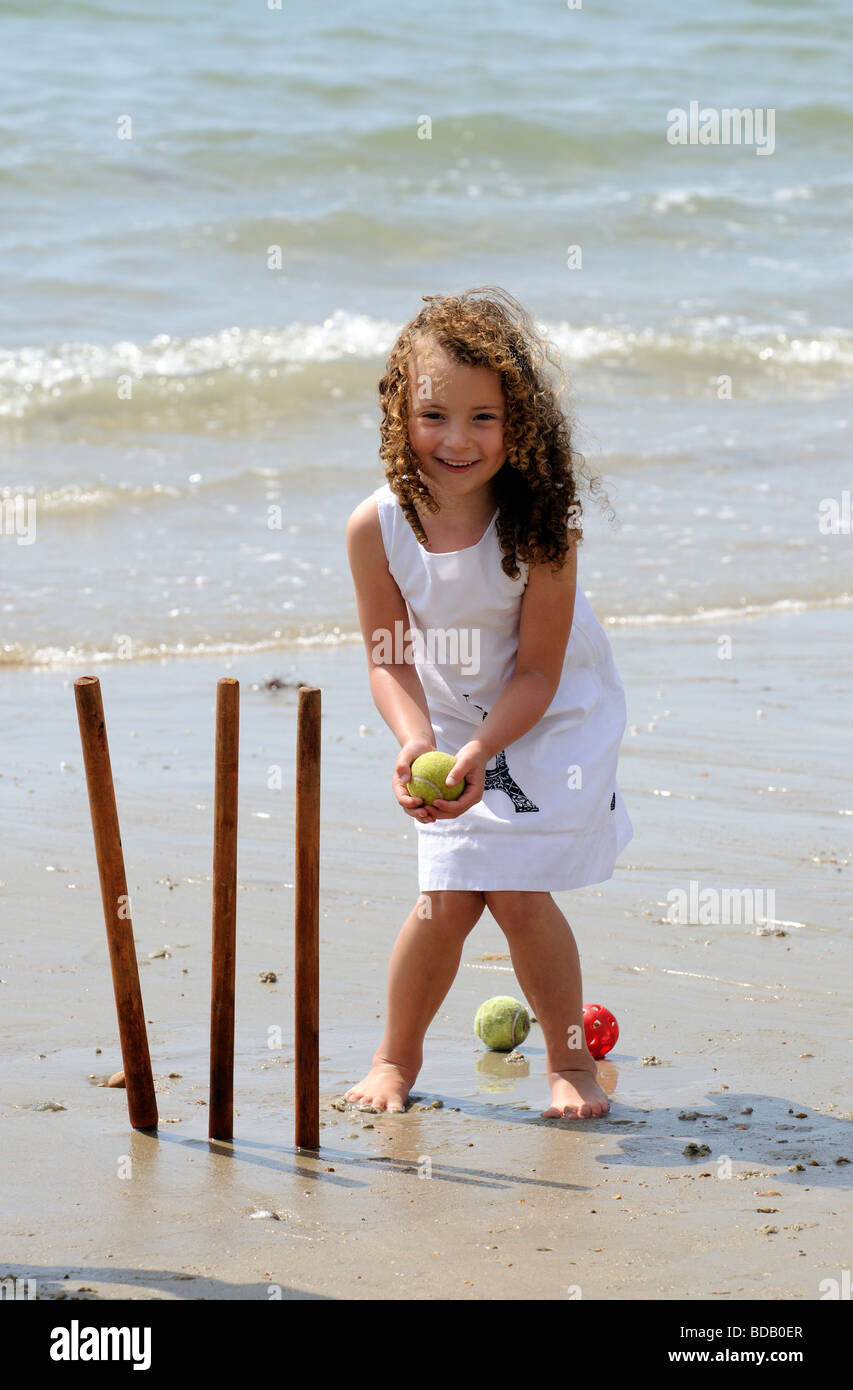 Little girl playing cricket catching a ball at the stumps during a holiday at the seaside Stock Photo