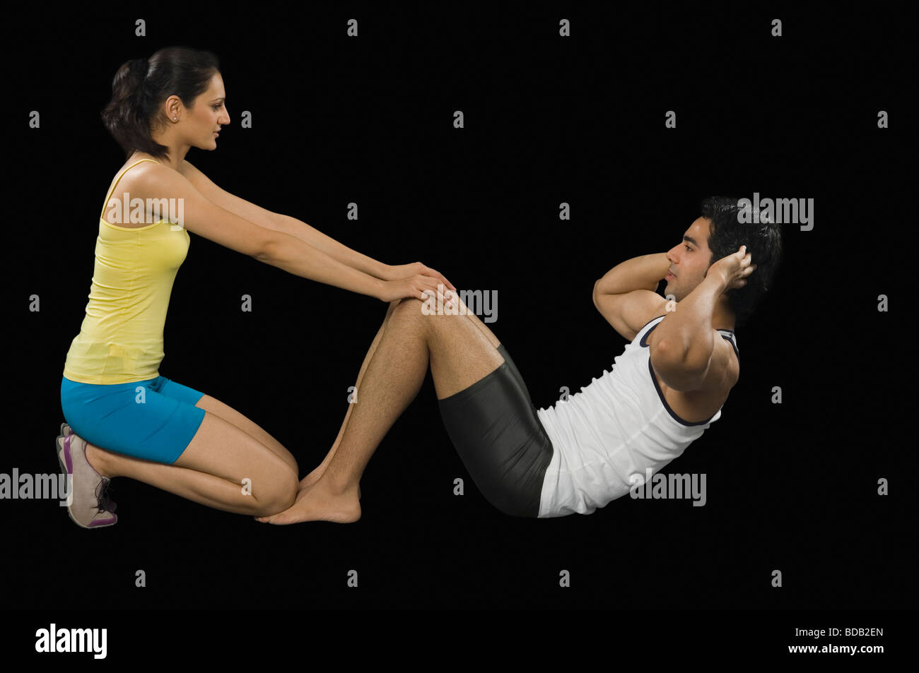 Female instructor helping man in doing sit-ups Stock Photo