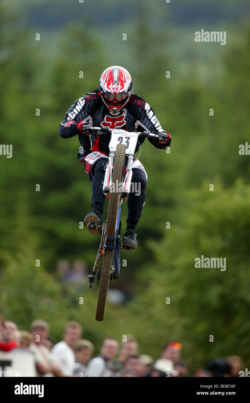 A Downhill Mountain Biker in mid air racing down a mountain course. Stock Photo